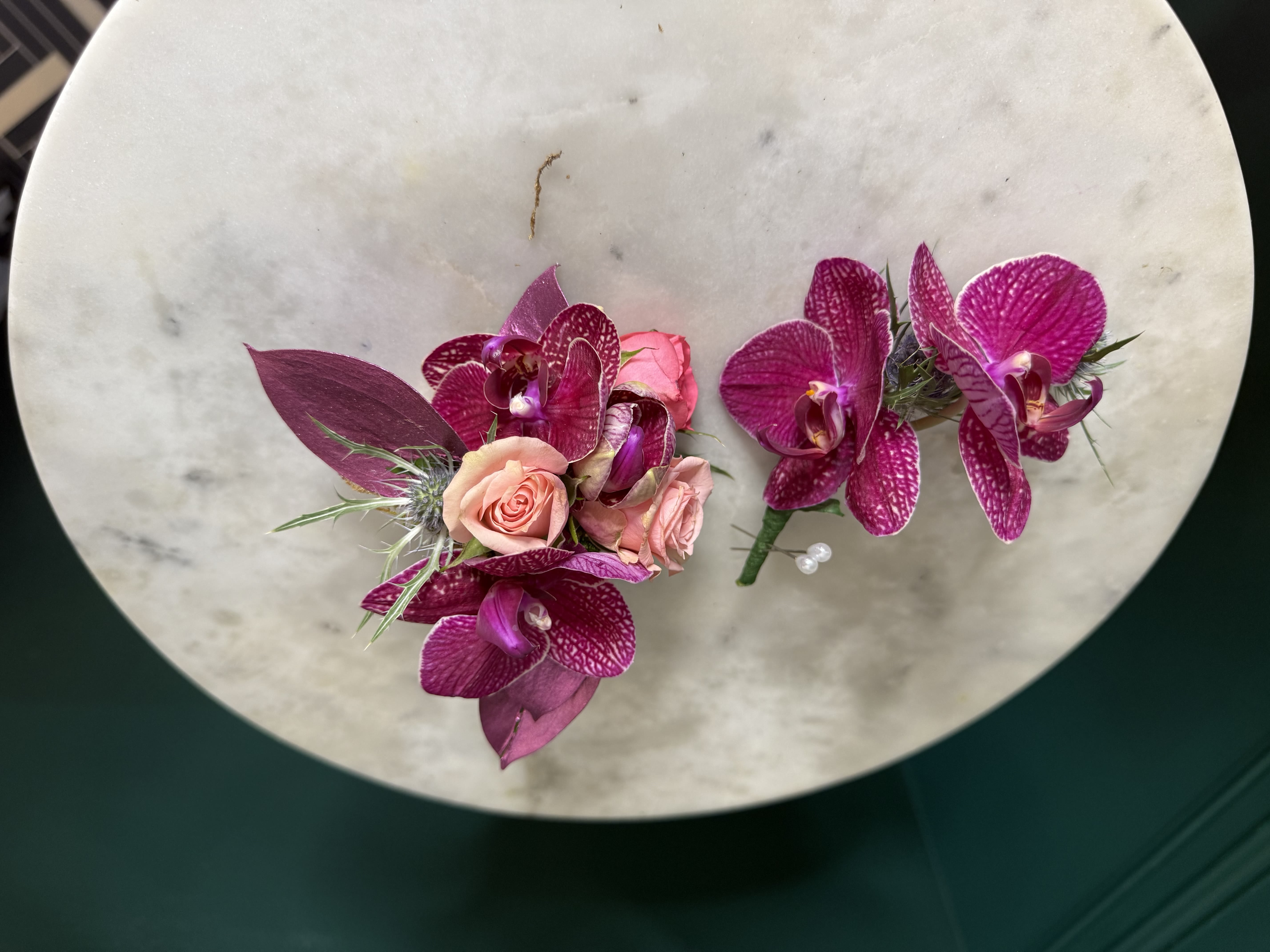 Pair of magenta orchid and peach rose boutonnieres on a round stone surface