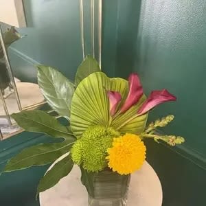 Modern arrangement with pink calla lilies and green and yellow blooms in a square glass vase
