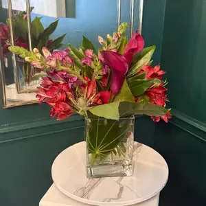 VIOLET NO. 1 - A striking, vertical composition featuring deep magenta calla lilies, purple and pink snapdragons, red alstroemeria, and a touch of textural blue thistle for contrast. Lush green foliage frames the blooms, creating a bold, architectural silhouette inside 