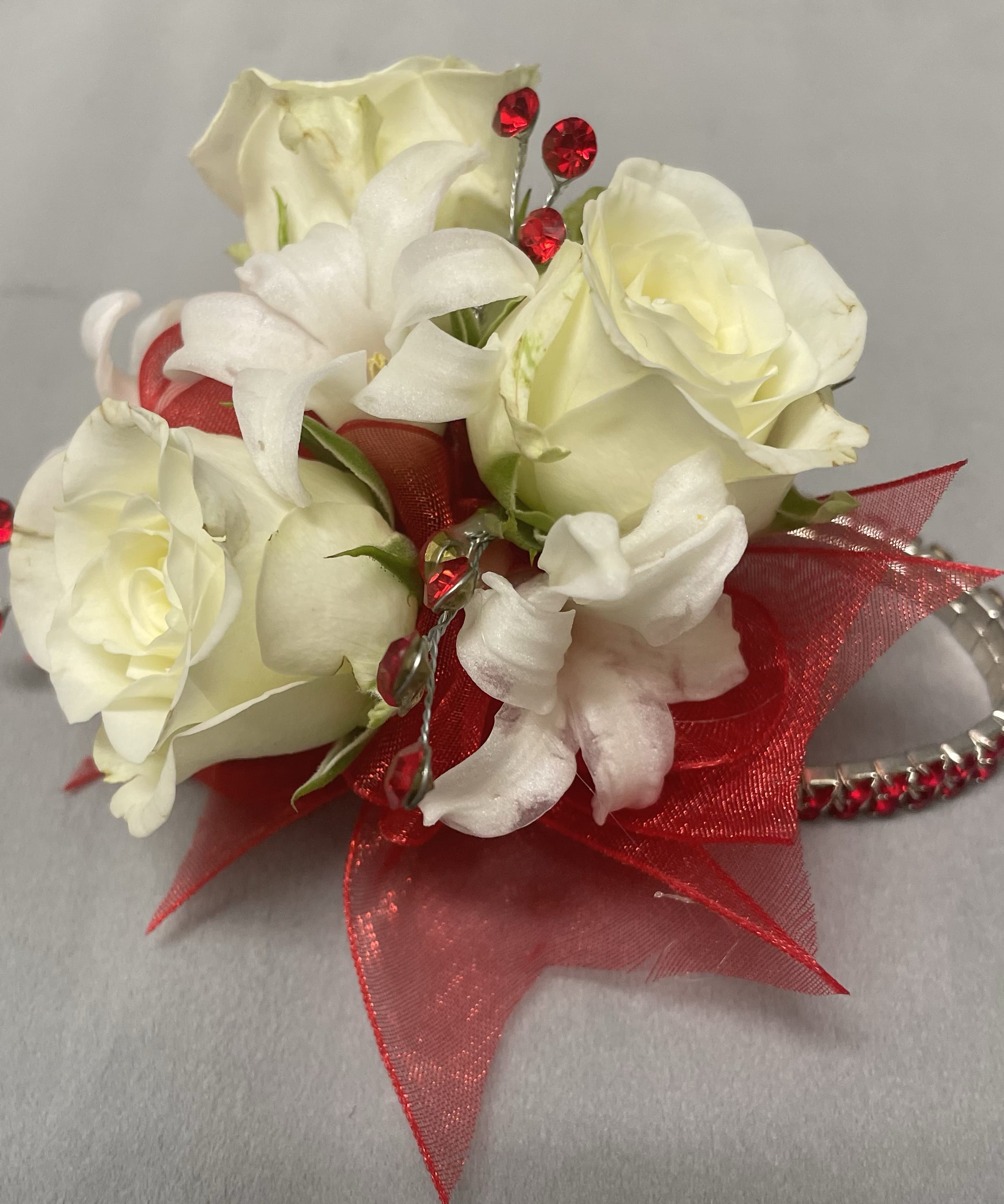 White rose wrist corsage with red ribbon and red rhinestones on a silver bracelet