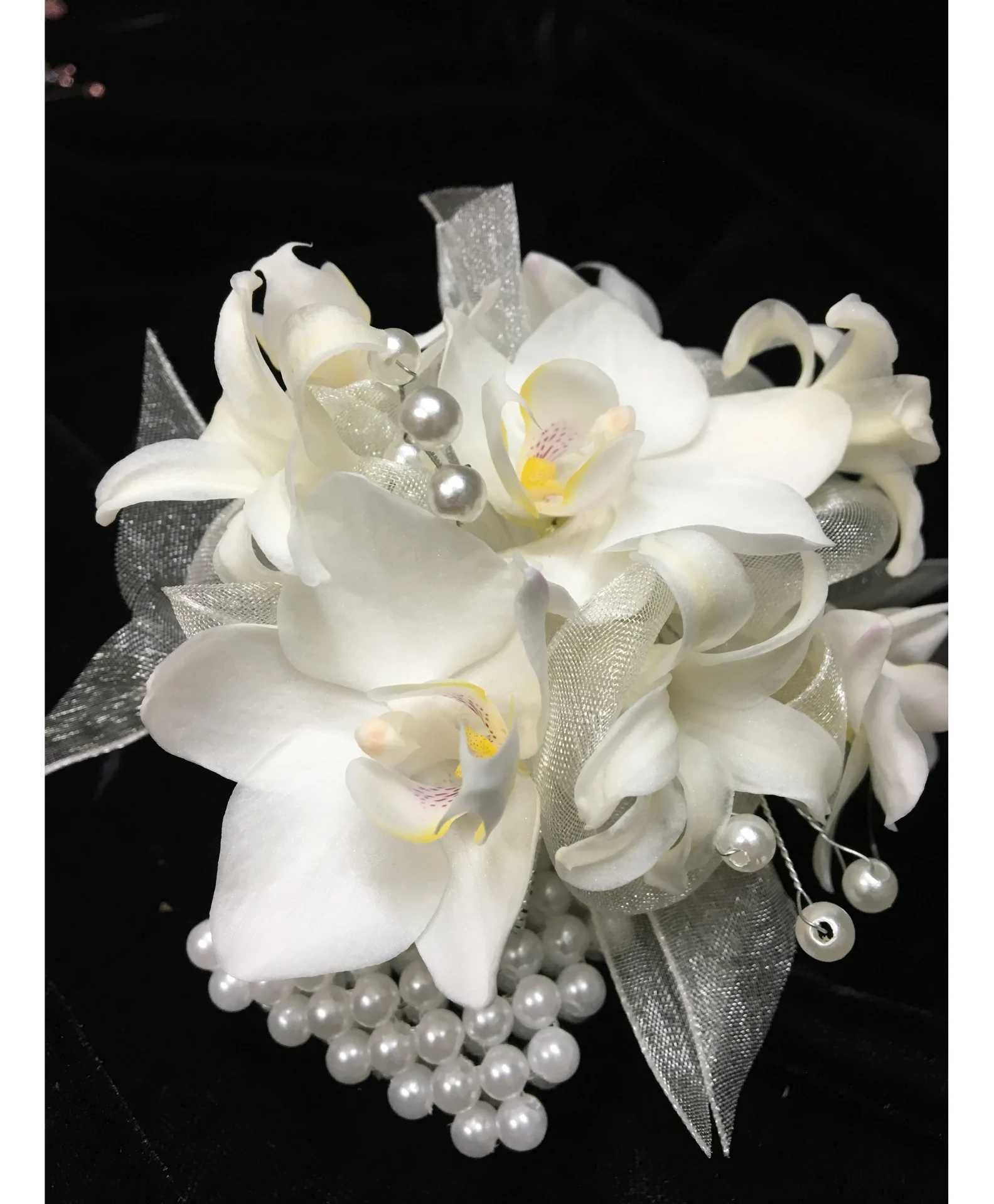 White orchid wrist corsage with silver ribbon and pearl accents on a black background