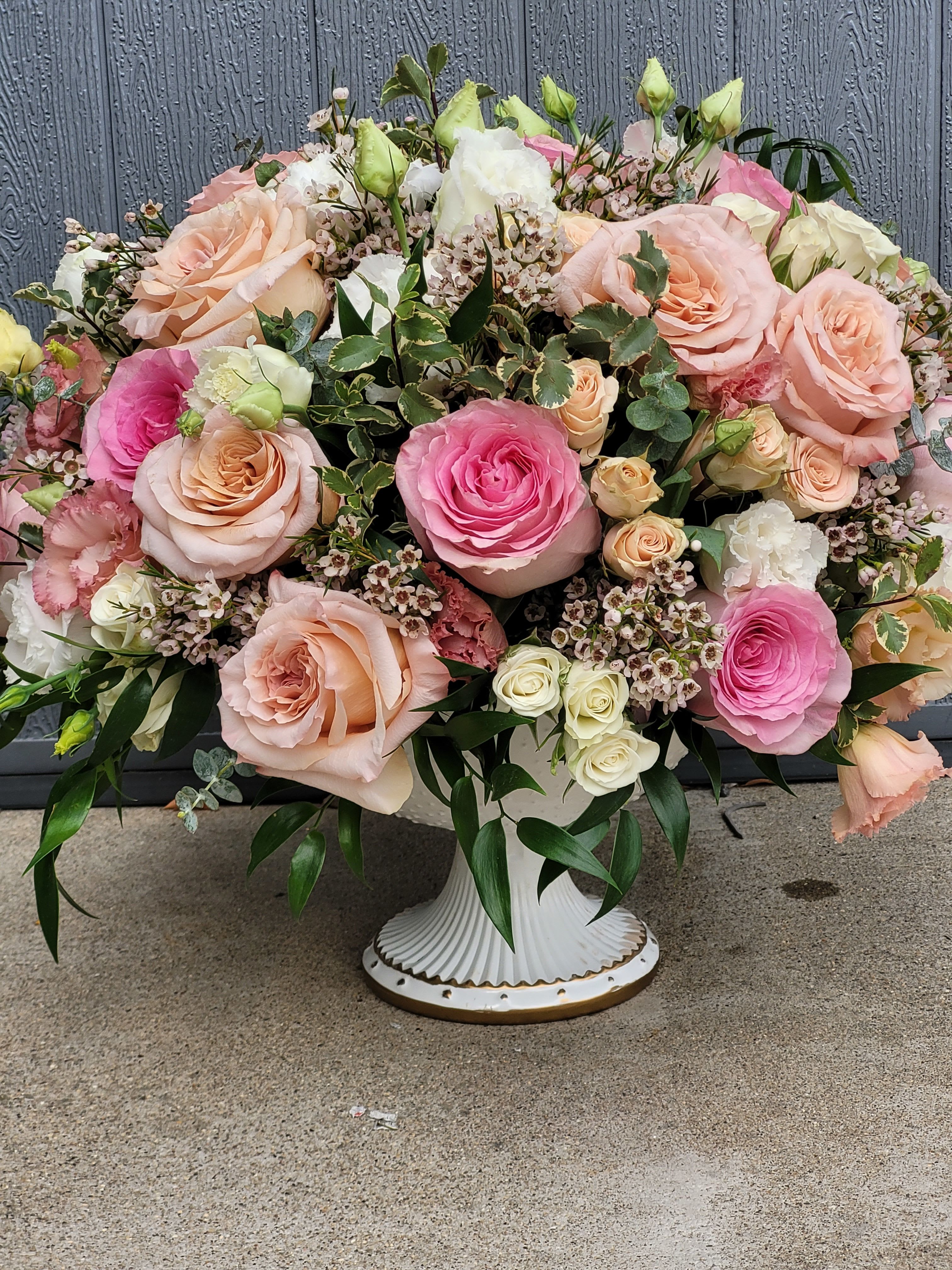 Low pedestal arrangement of peach and pink roses with white accents in a white compote vase