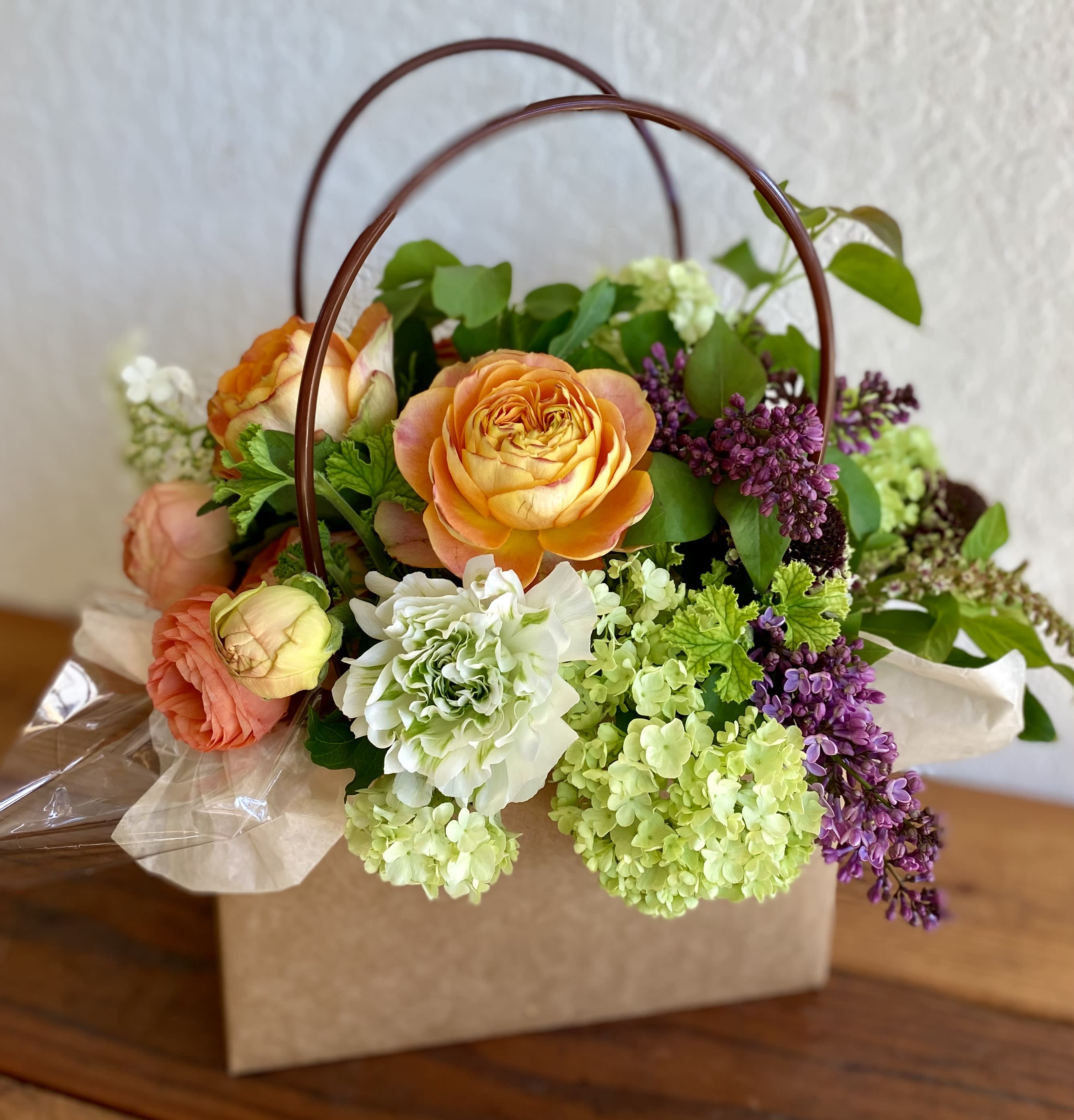 Peach roses, green hydrangeas, and purple flowers in a kraft box with curved handles