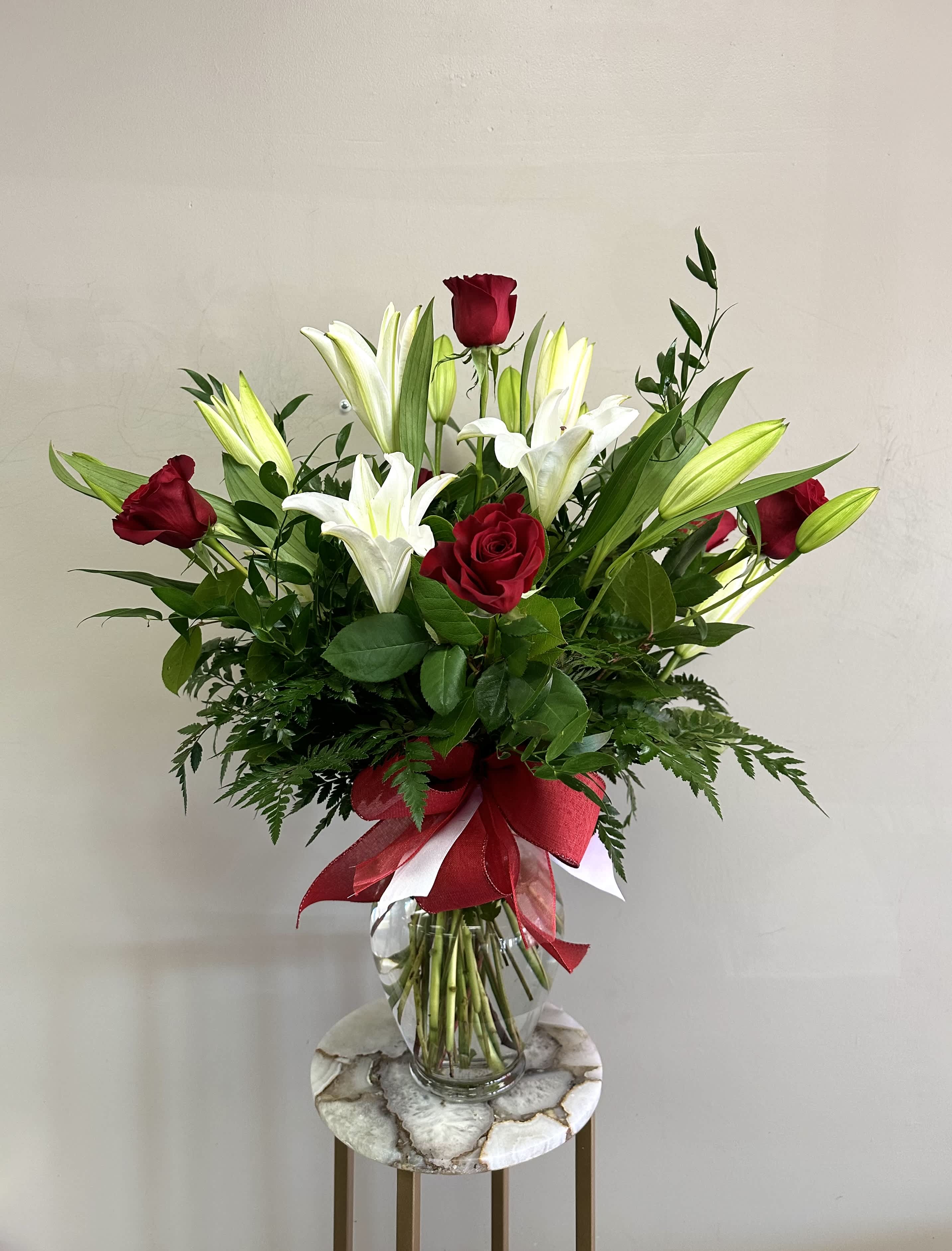 Tall arrangement of red roses and white lilies in a clear vase with a red bow.