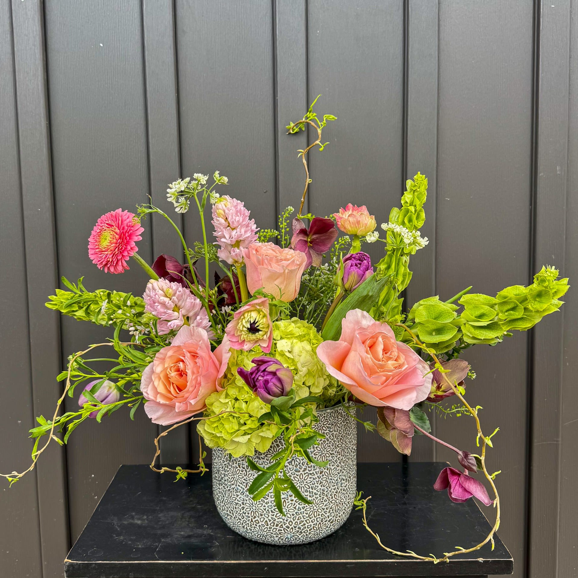 Nature Song - A Spring Celebration in a vase! This arrangement is full of bright greens, purples, pinks and peaches in a beautiful textured ceramic vessel.
