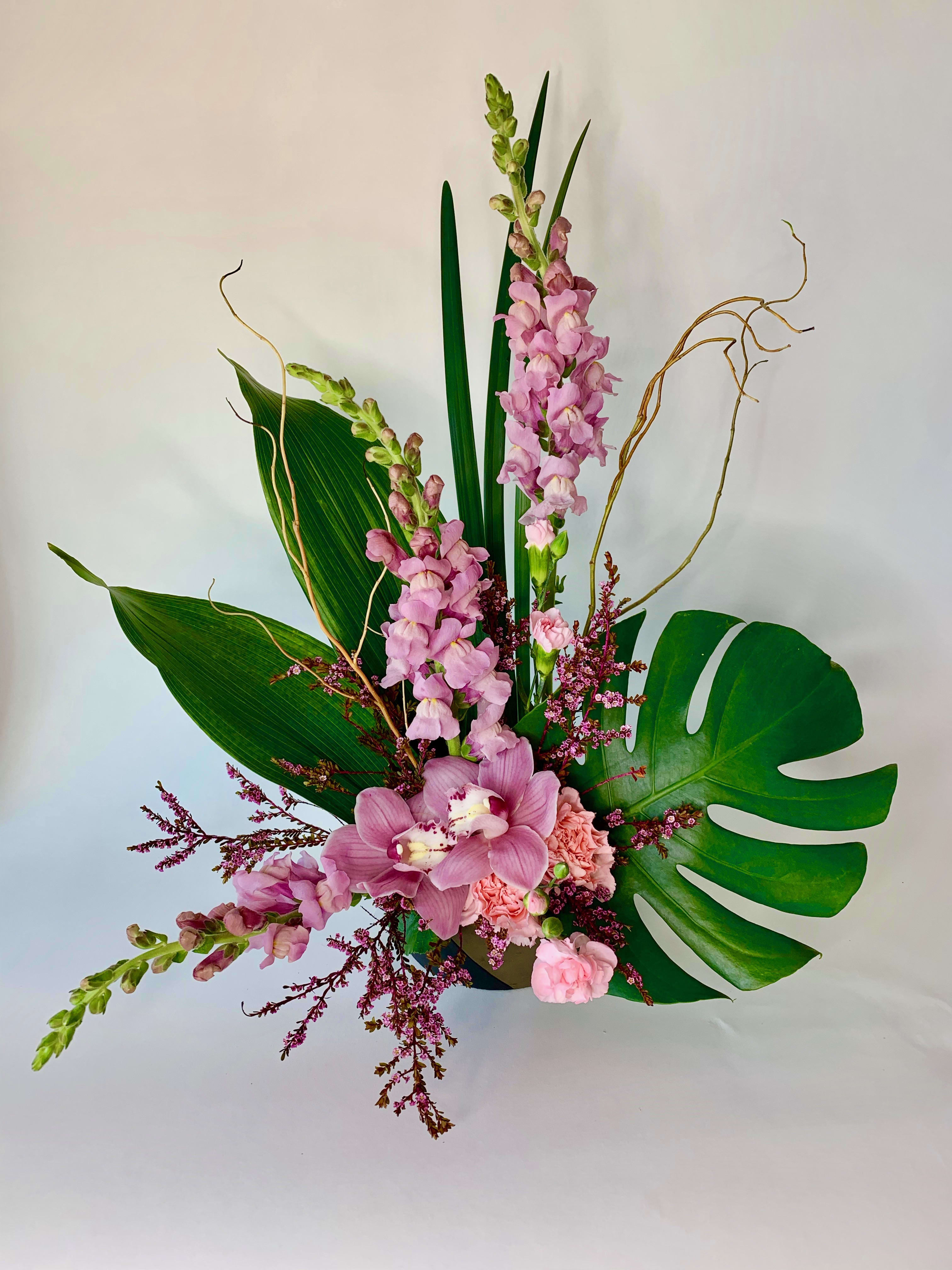 Imagination Blooms  - The exotic bouquet includes pink cymbidium orchids, light pink carnations, pink Snapdragons  and accented with ti leaves and other assorted greenery.