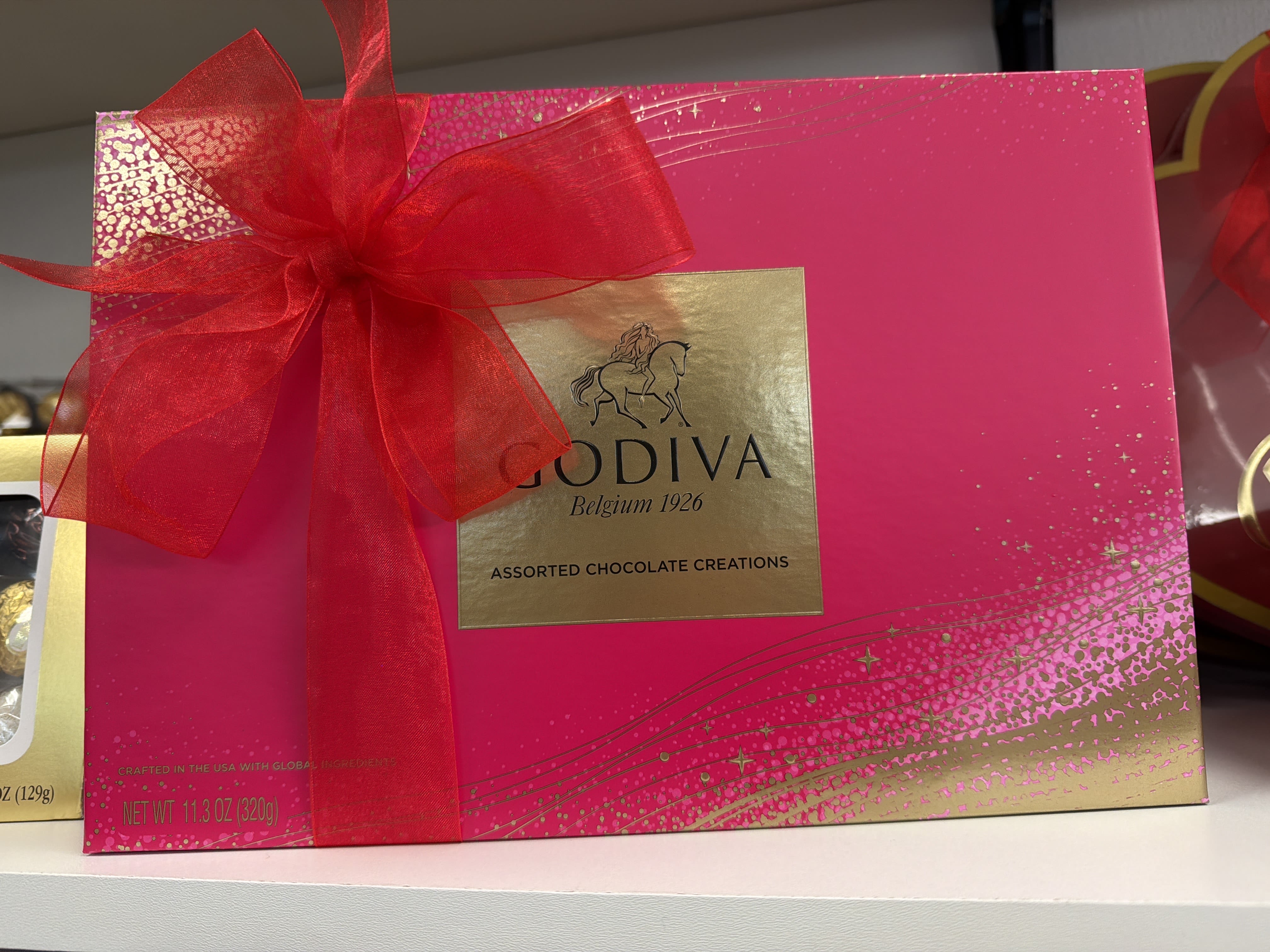 Bright pink Godiva assorted chocolates gift box with gold label and large red ribbon bow