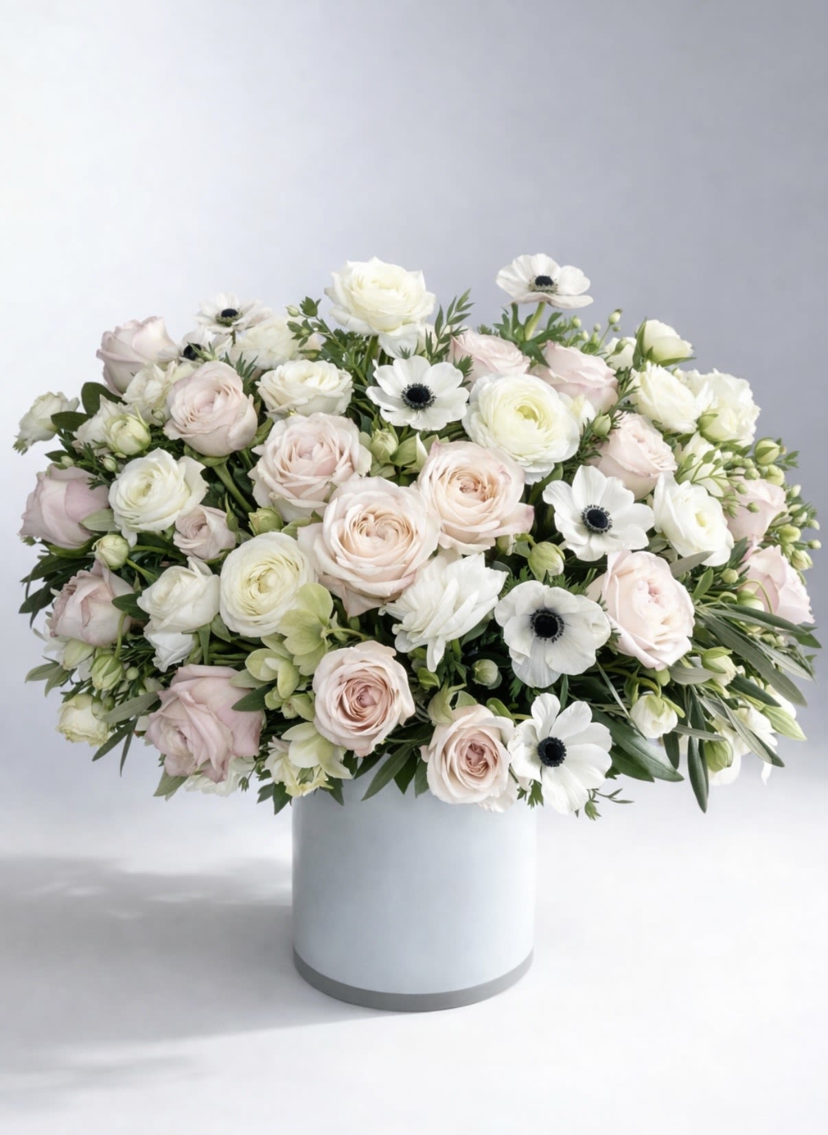 Spring Equinox - A graceful study in softness and sophistication, this refined arrangement features blush garden roses, creamy ranunculus, delicate white anemones, and fresh seasonal botanicals artfully composed in a modern vessel. Airy yet abundant, it brings a sense of calm luxury to any space.  Designed for those who appreciate understated beauty, this piece makes an exceptional Mother’s Day gift, an elegant gesture for the home, or a polished offering for meaningful occasions. Its soft palette and sculptural form feel both timeless and elevated—perfect for a kitchen island, entryway, or bedside table.  Details: Premium seasonal blooms in blush, ivory, and soft green Lush, garden-inspired styling with an elegant, tailored finish  A beautiful expression of love, gratitude, and quiet luxury.  *photo shown in premium version
