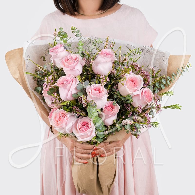 Large bouquet of light pink roses with small pink filler flowers wrapped in kraft and tissue paper