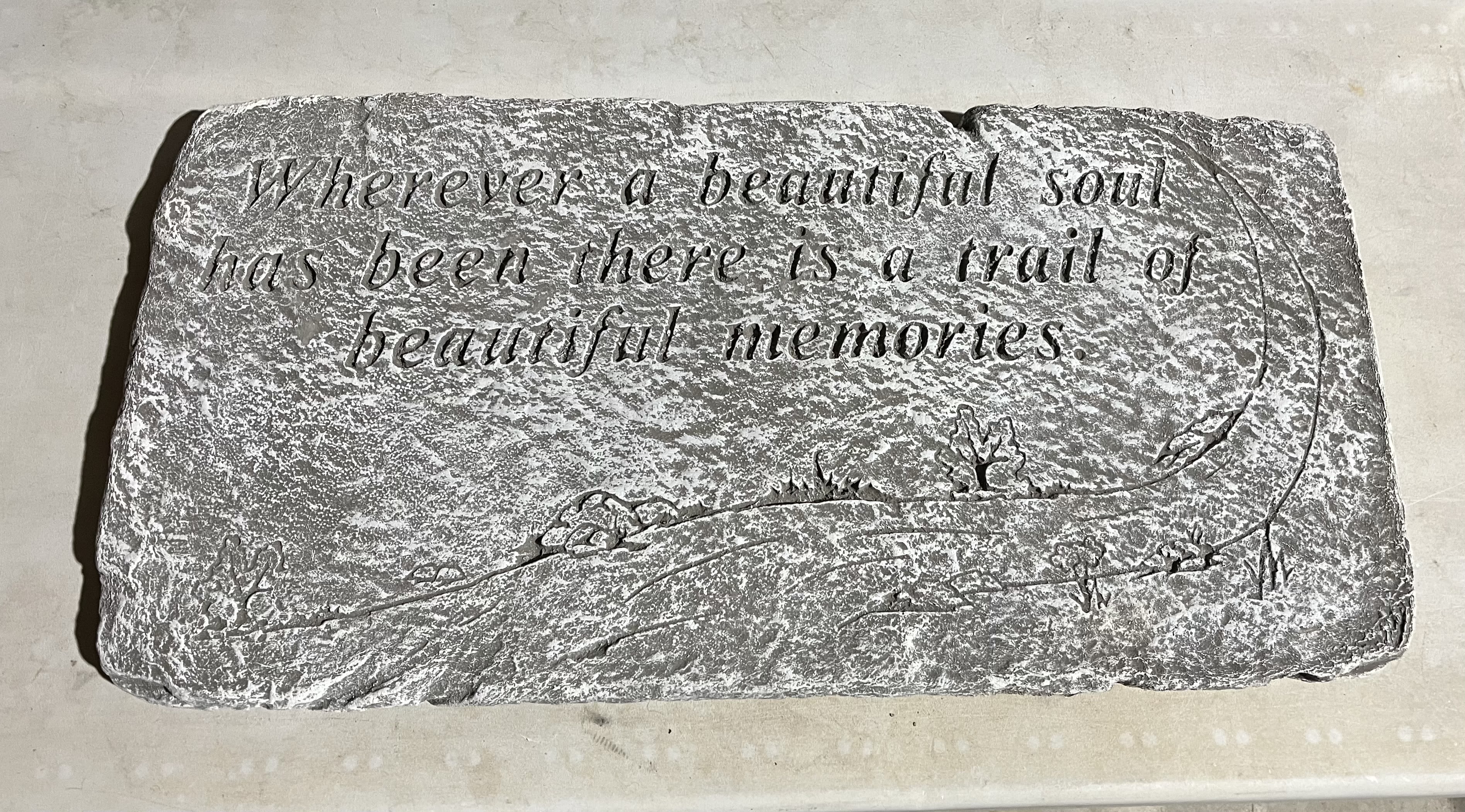 Rectangular gray memorial stone engraved with a sentimental quote and small landscape motifs.