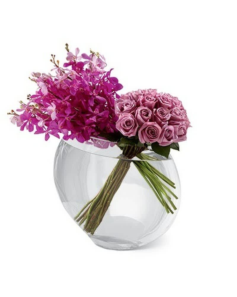 Modern arrangement of pink orchids and lavender roses in a clear round glass vase