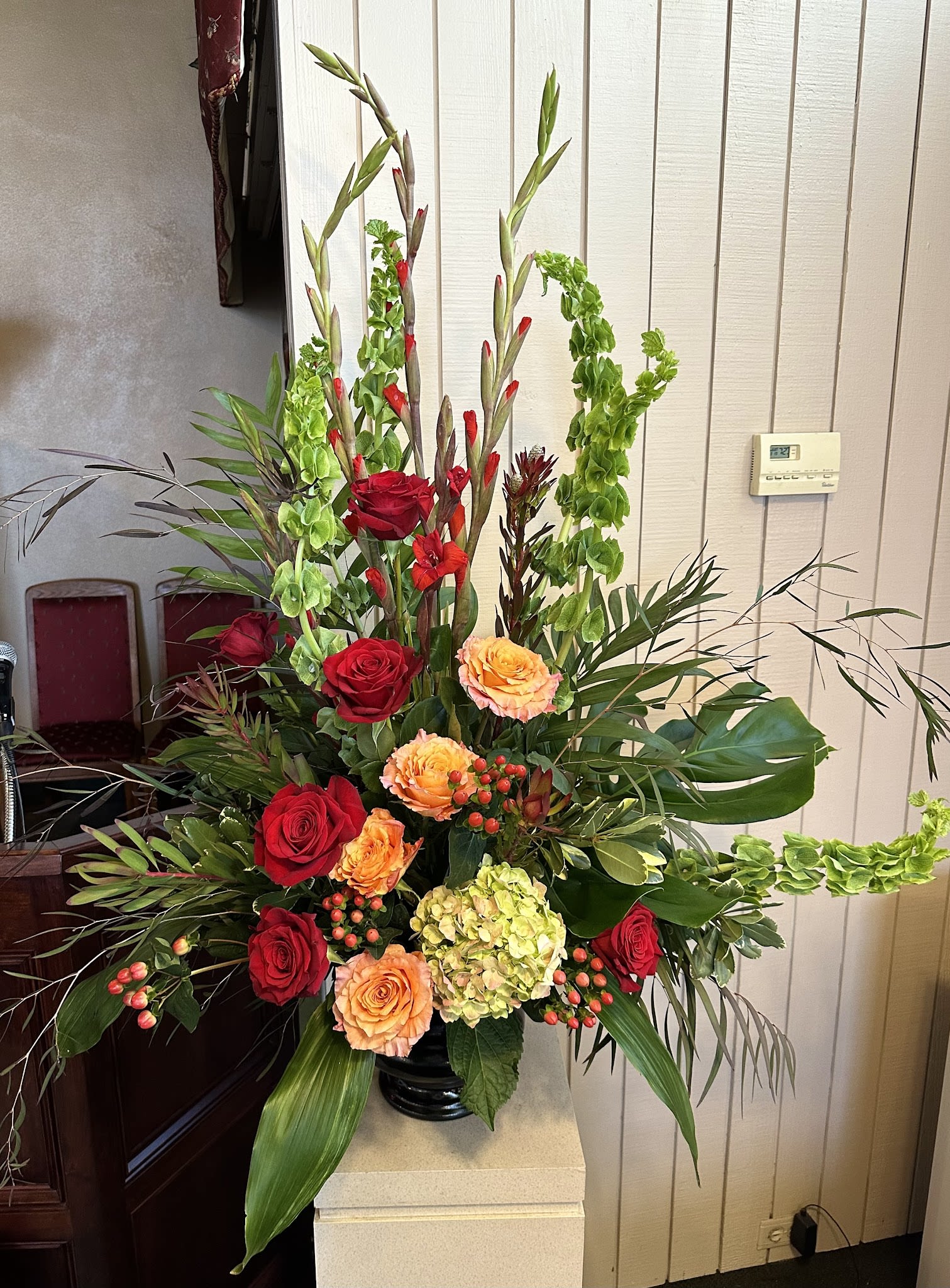 Tall arrangement of red and peach roses with green hydrangea and Bells of Ireland in a black vase