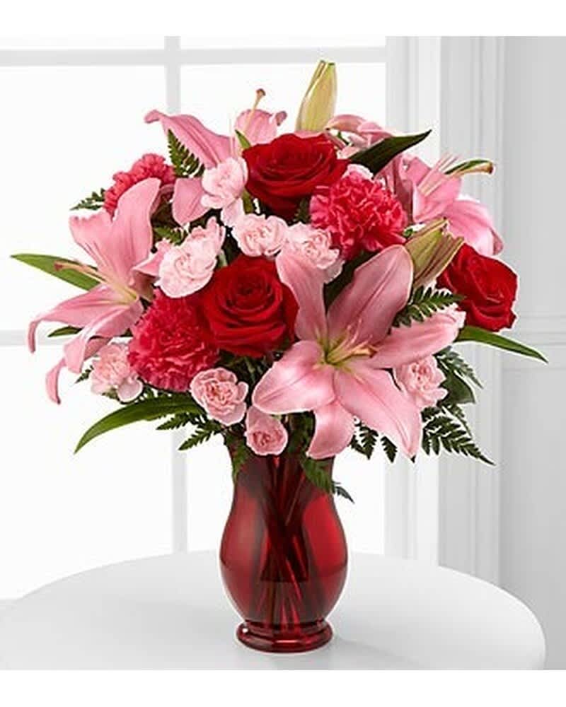 Arrangement of pink lilies, red roses, and pink carnations in a red glass vase