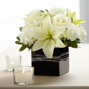 Low white lily and rose arrangement in a black square vase with votive candles