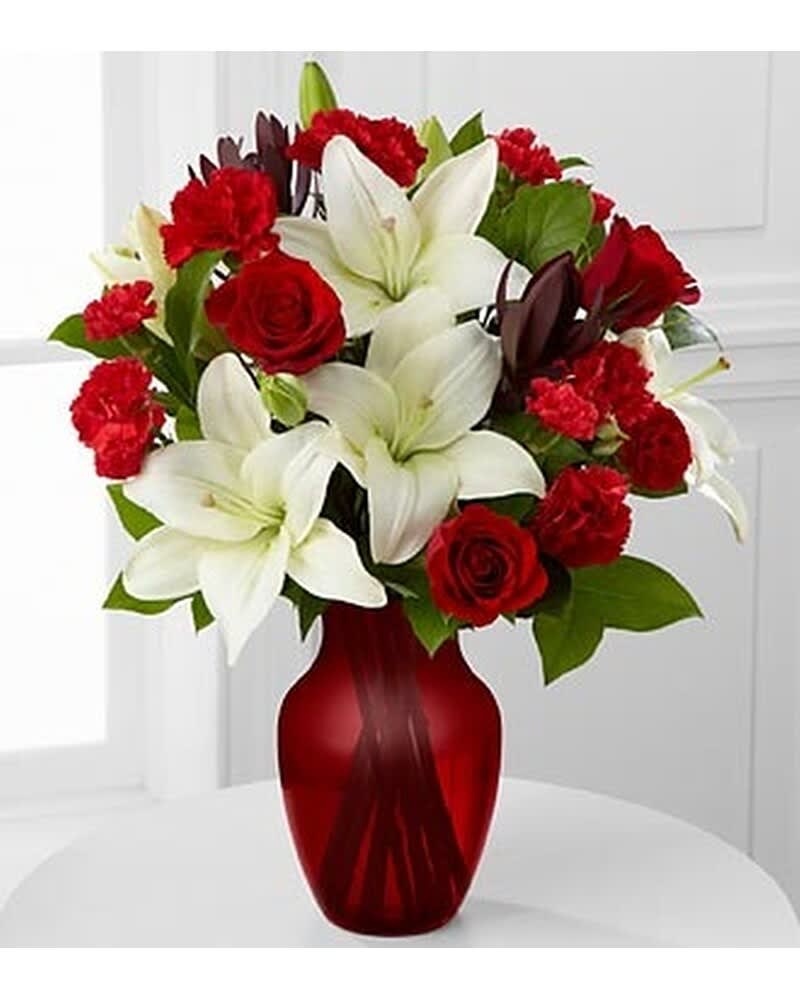 Arrangement of white lilies, red roses, and red carnations in a red glass vase.