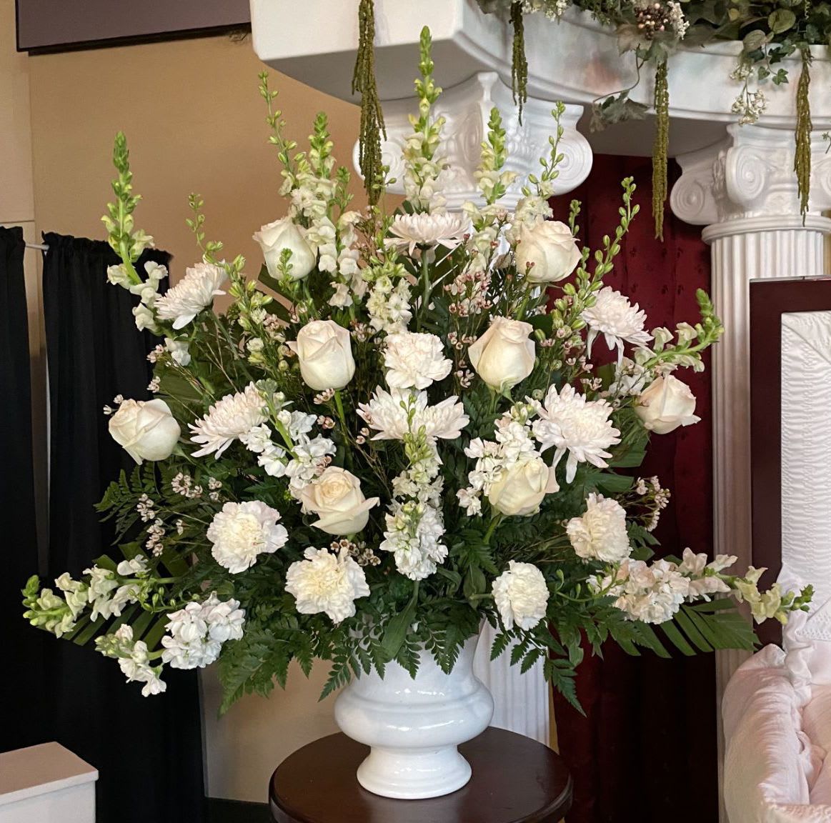 Large white arrangement of roses, carnations, and chrysanthemums in a white urn-style vase