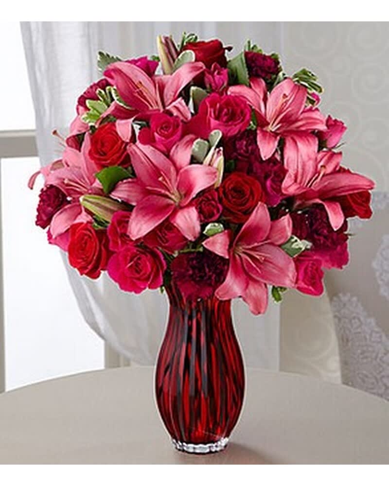 Arrangement of pink lilies and red roses in a red glass vase
