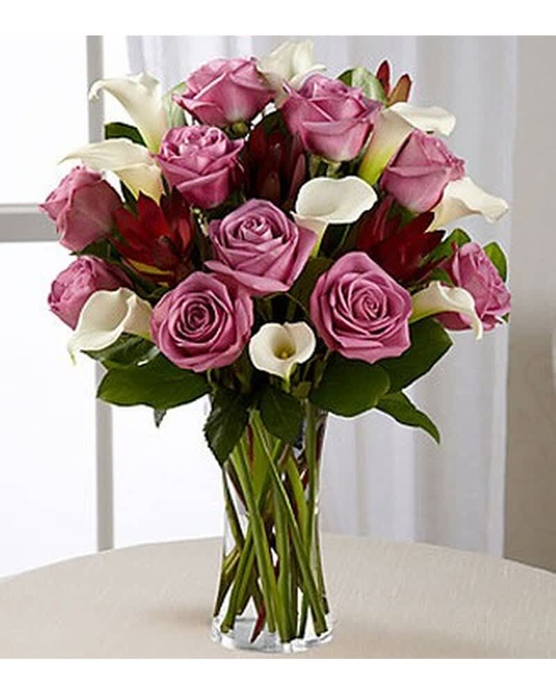 Tall glass vase of lavender roses, white calla lilies, and red accent blooms