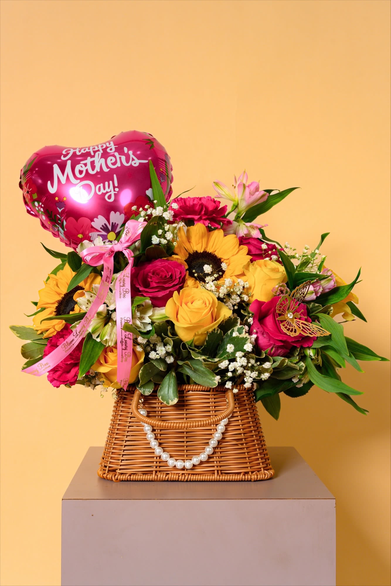 Sunlit Love Basket - Bursting with cheerful sunflowers, golden roses, and vibrant pink accents, this arrangement radiates warmth and joy. The playful Mother's day balloon and charming details add a festive, heartfelt touch. It's a bright celebration of love, perfect for making any mother feel truly special.