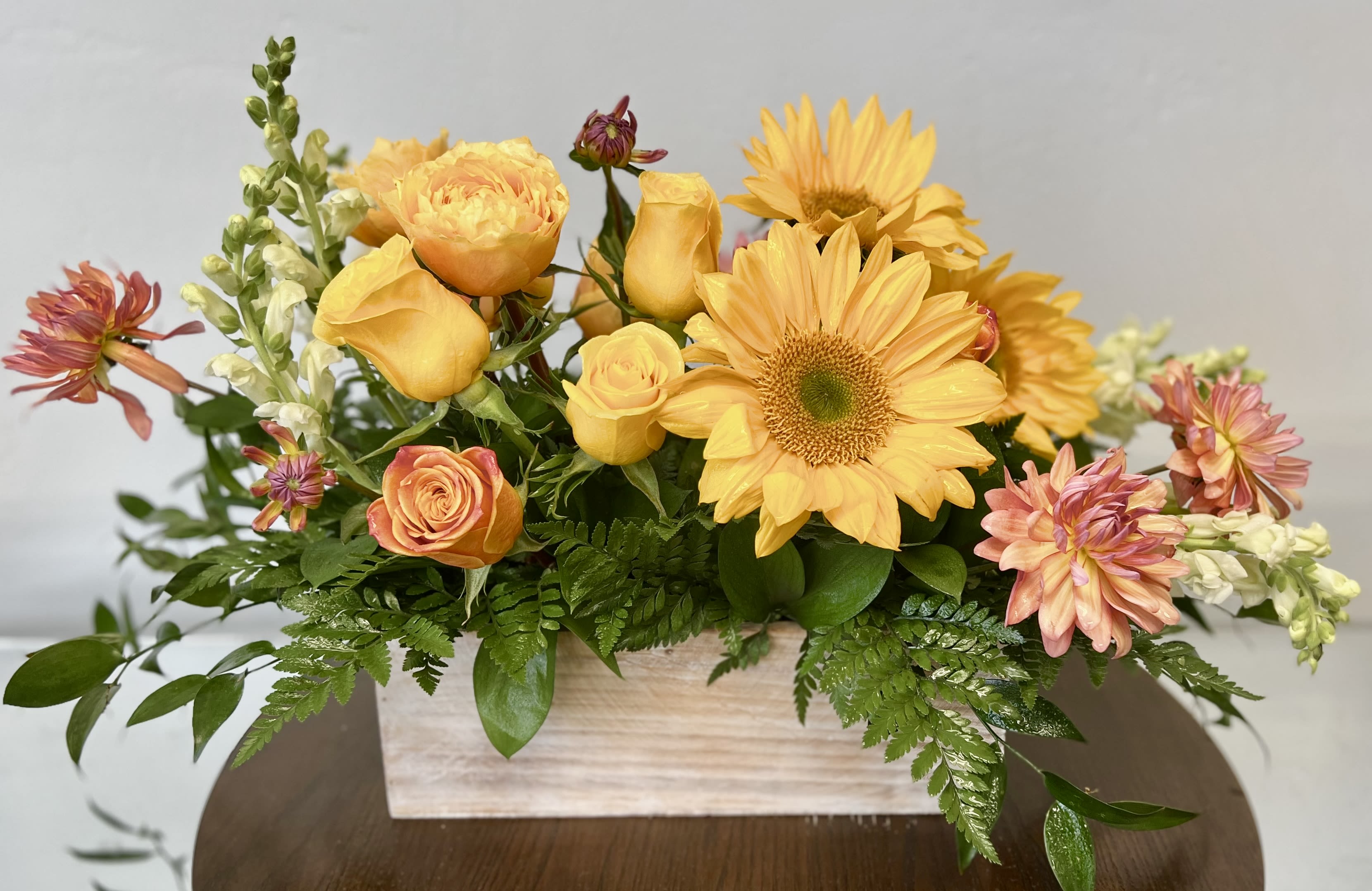 Low yellow and peach floral arrangement with sunflowers and roses in a rectangular wooden box