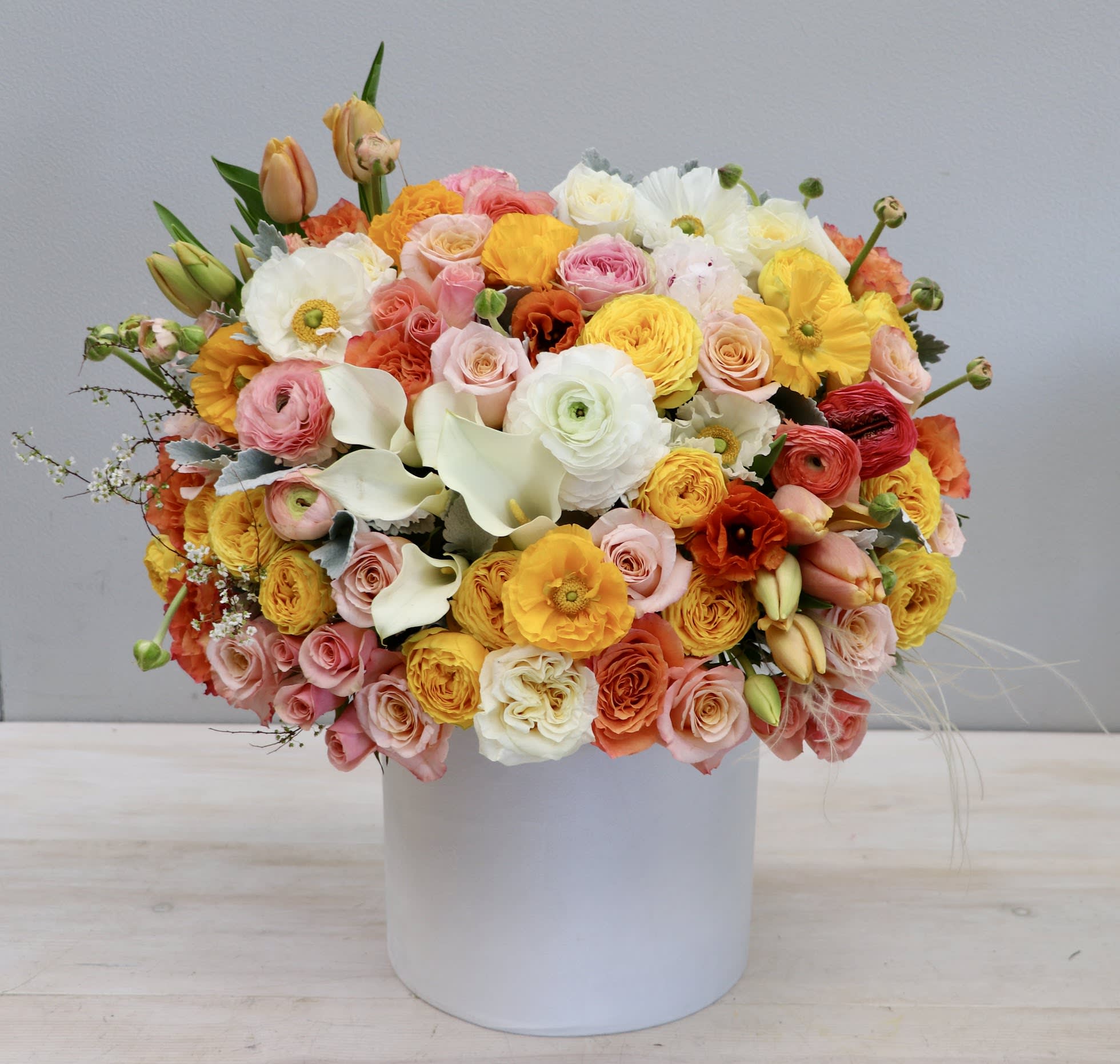 Round arrangement of pink, yellow, orange, and white flowers in a white hatbox-style container.