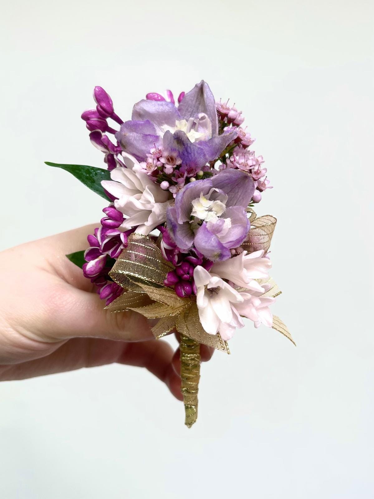 Small handheld boutonniere of purple and pink flowers with a gold ribbon-wrapped stem.