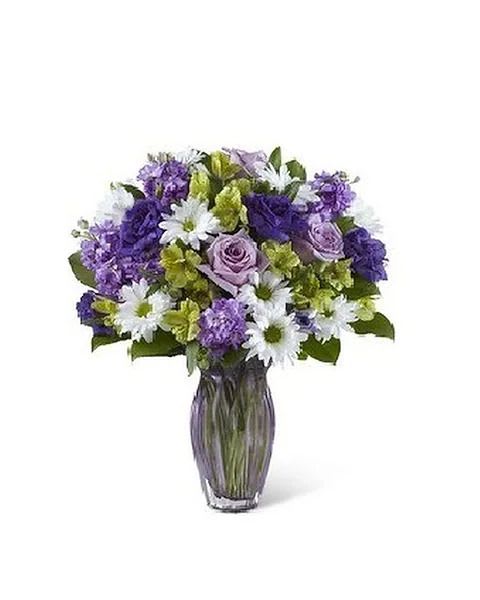 Loving Thoughts Bouquet - Purples in shades from pale pastels to plum pop perfectly among green alstroemeria and white daisy poms. For any Mom that has a passion for the calming, peaceful, mysteries of purple, this bouquet is made to order and is sure to be long-remembered. This brilliant gathering of stock, lisianthus, daisy poms, roses is hand-arranged in a heavy, lilac-hued heirloom quality glass vase and makes an outstanding way to endow any day with "special occasion" status. 