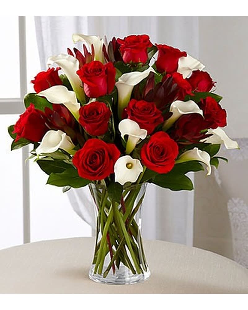 Arrangement of red roses and white calla lilies in a clear glass vase on a light table