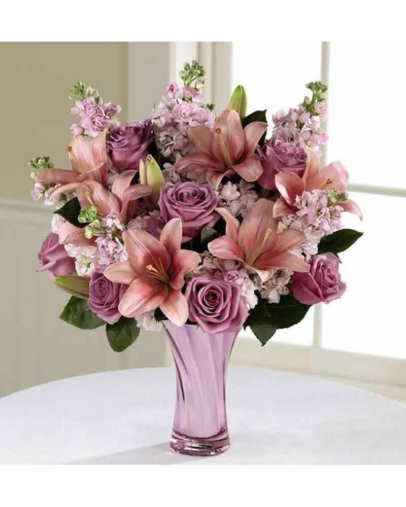 Pink lilies and purple roses arranged in a lavender glass vase