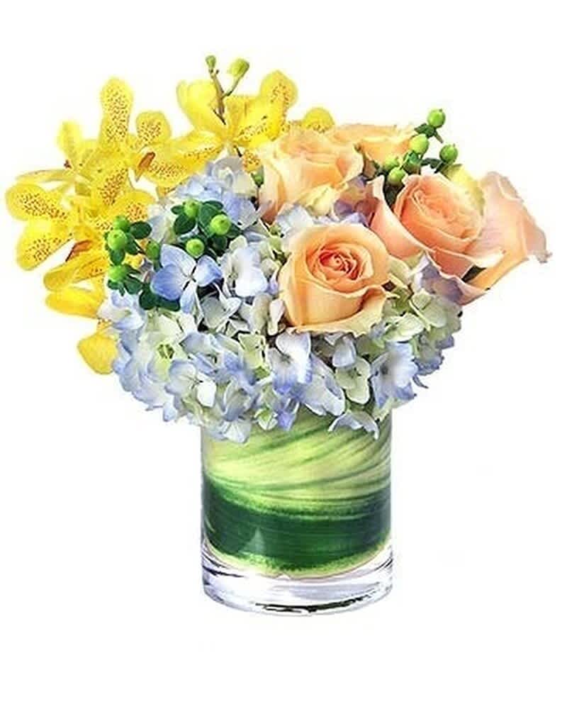 Compact arrangement of peach roses, blue hydrangeas, and yellow orchids in a glass vase with green leaf wrap.