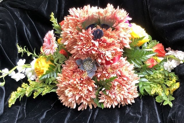 Puppy Love - A cuddly floral puppy crafted from tightly clustered peach chrysanthemums, this playful flower arrangement is a birthday-ready delight that also suits new baby celebrations, get-well wishes, or a sweet "just because" surprise. The character-shaped design-the puppy's head, body and limbs rendered in soft peach blooms-creates an immediate warm, whimsical impression that will make the person you're thinking of smile and feel genuinely seen.  Dark bead accents form the bear's eyes and nose for charming detail, while a pink ribbon collar, fabric bow and jeweled brooch add a polished, gift-ready touch. Bright yellow roses, pink gerbera-style blooms and small white accents fan around the bear like a floral collar against a dark fabric backdrop, giving the arrangement a cheerful pop of color and texture. Ideal for celebrating a newborn, cheering up someone under the weather, or sending romantic affection with a playful twist-this piece arrives fully dressed and ready to delight.