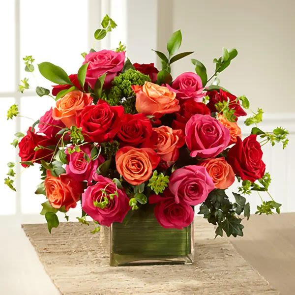 Sunset Romance - A lush and vibrant arrangement featuring premium roses in rich shades of red, hot pink, and coral, accented with fresh greenery in a modern glass cube vase. Sunset Romance is full of color and elegance, making it a beautiful choice for birthdays, anniversaries, Mother’s Day, or simply to brighten someone’s day.  Please note: Flower varieties and shades may vary based on seasonal availability. Substitutions may be made with flowers of equal or greater value while maintaining the overall style and color palette of the arrangement.