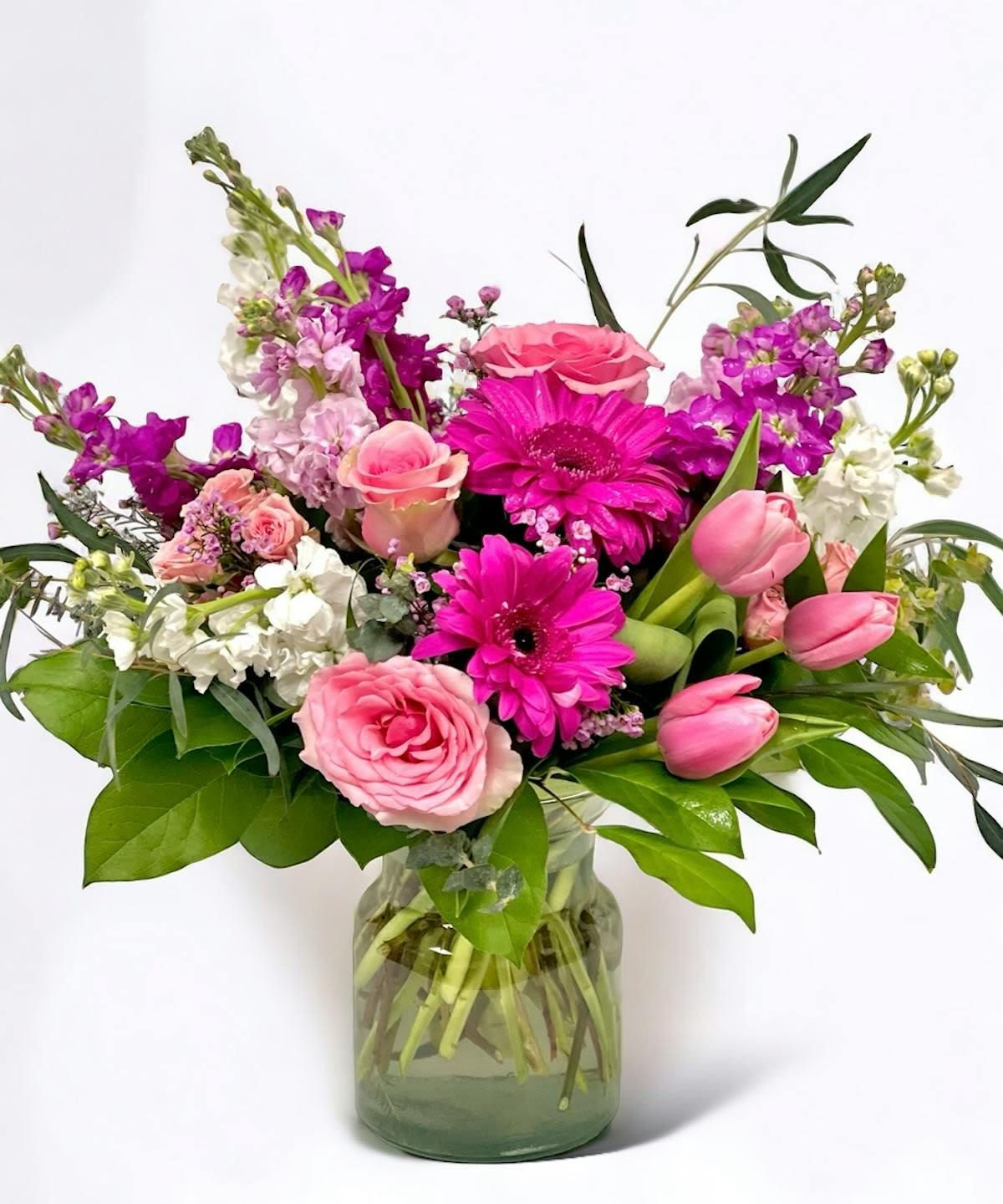 Blushing Garden - A cheerful garden-inspired bouquet featuring soft pink roses, tulips, vibrant gerbera daisies, stock, and seasonal accent blooms gathered in a clear glass vase. Blushing Garden is filled with fresh spring color and natural texture, making it perfect for birthdays, Mother’s Day, get well wishes, or simply brightening someone’s day.  Please note: Flower varieties and colors may vary due to seasonal availability. Substitutions may be made with flowers of equal or greater value while preserving the overall look, feel, and color palette of the arrangement.