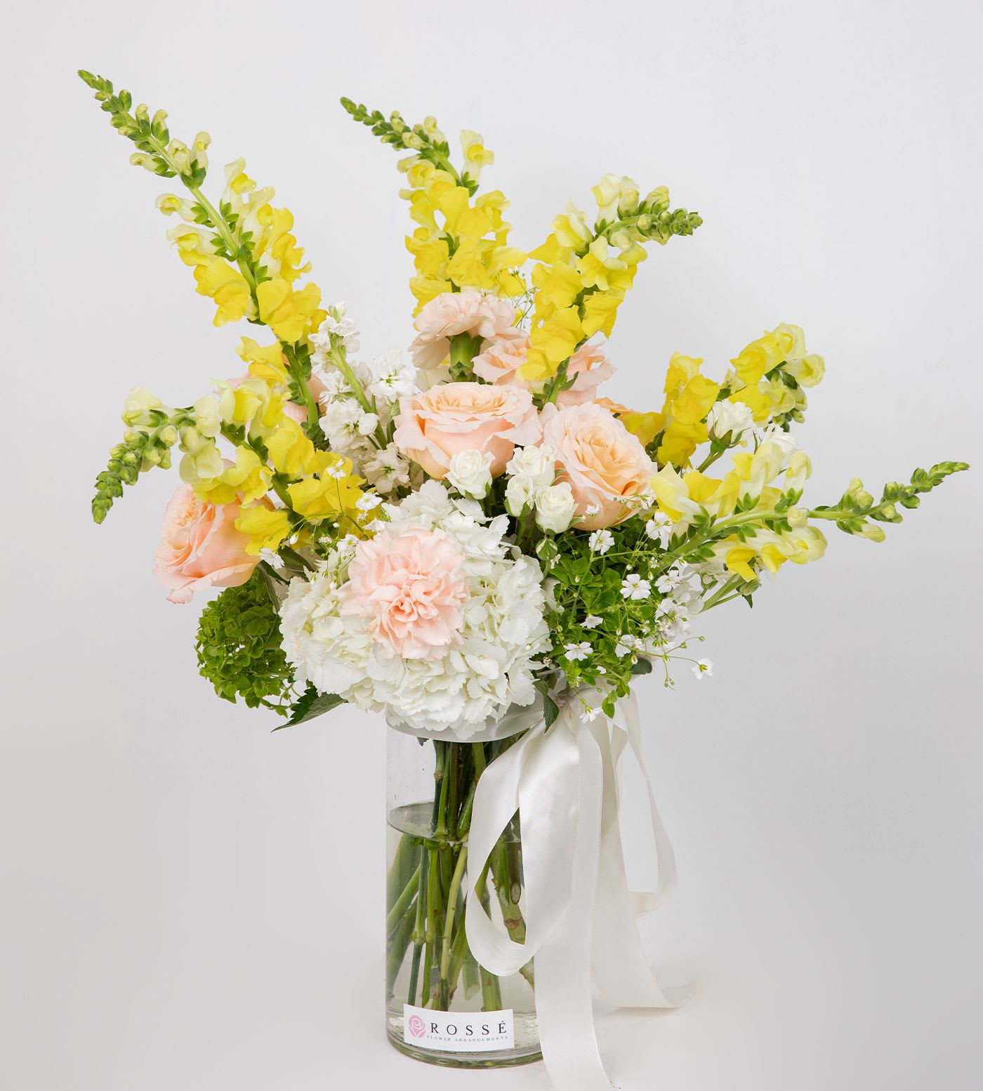 Sunny - A soft and cheerful vase arrangement in peach, white, and yellow tones, designed in a clear glass vase and finished with an elegant ivory ribbon.  Perfect for brightening any occasion.