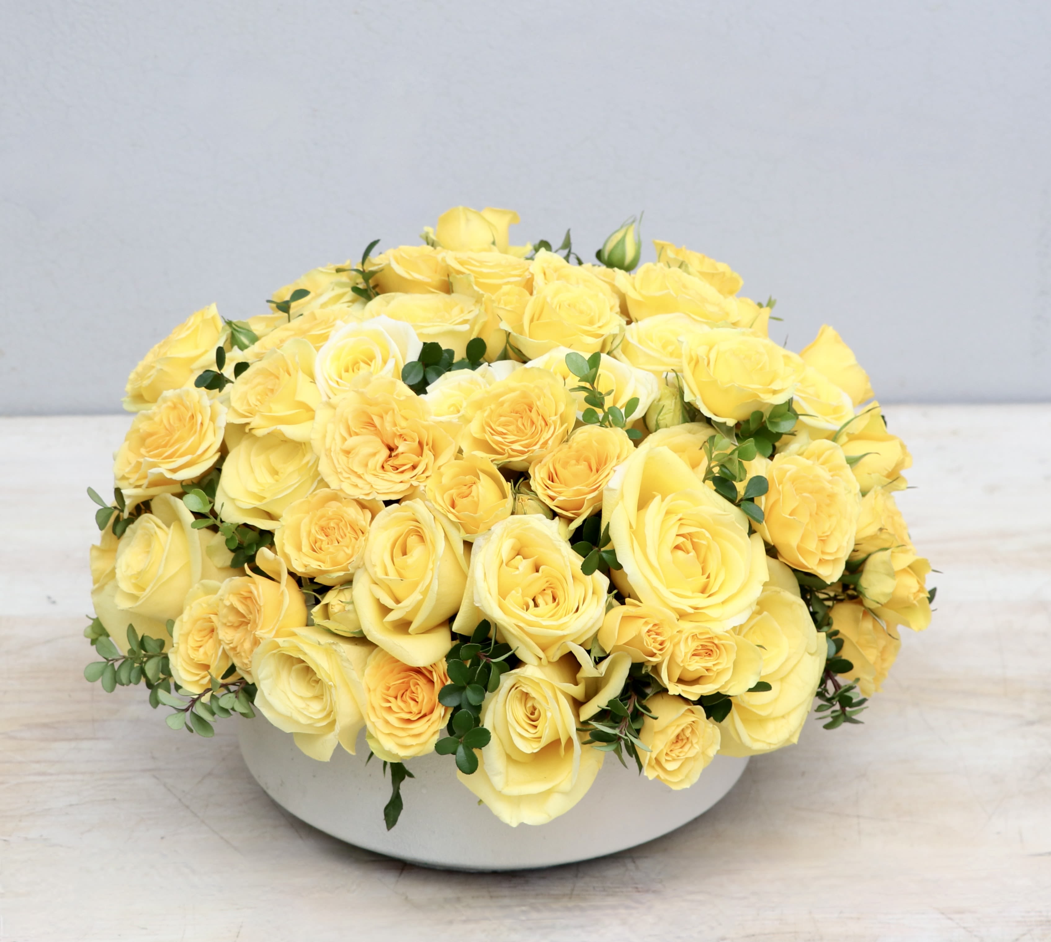Low round arrangement of yellow roses in a white bowl-shaped container