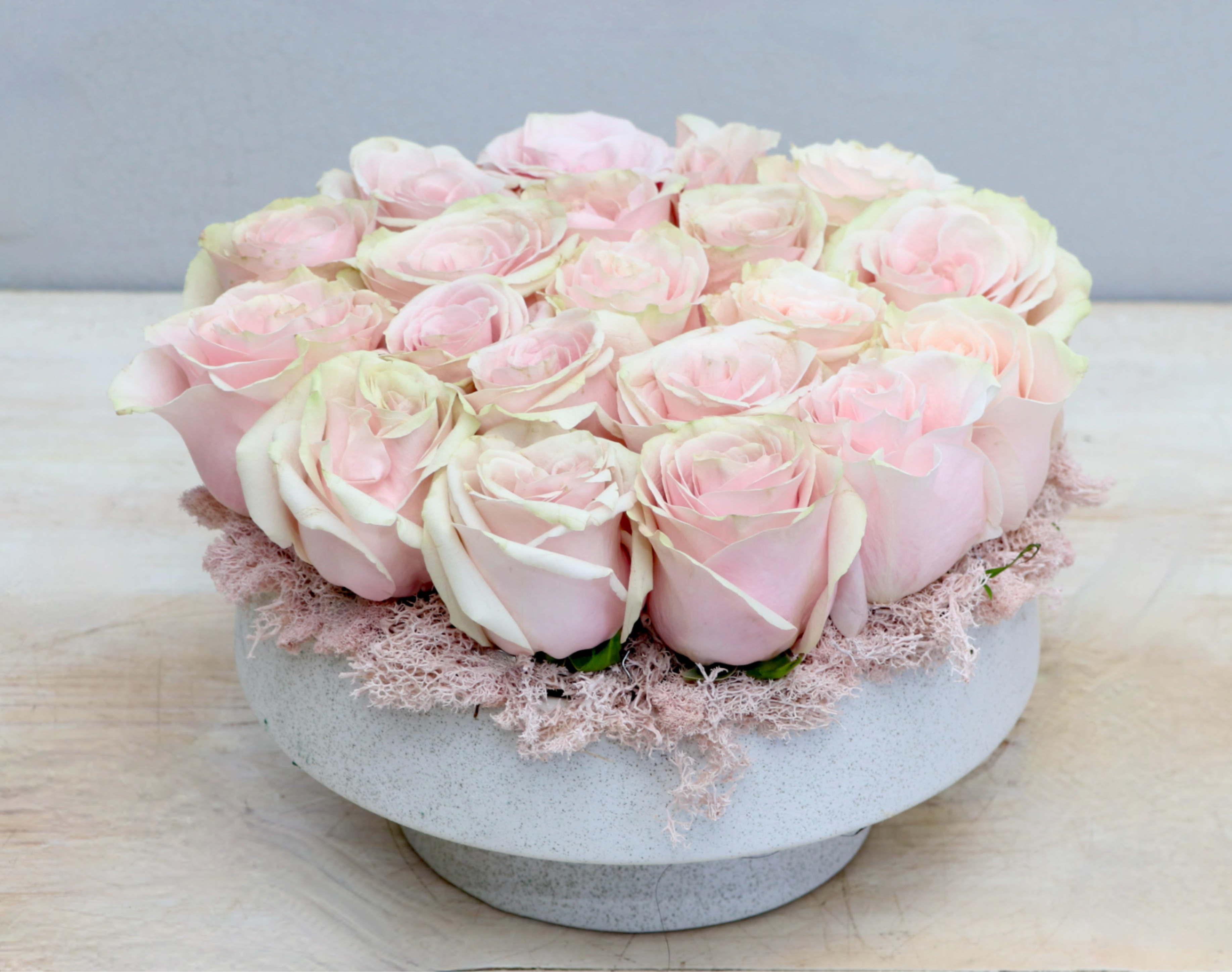 Low round arrangement of pale pink roses tightly packed in a white bowl