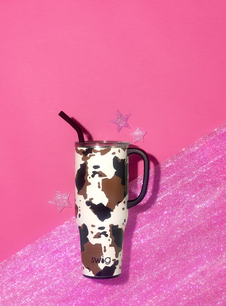 Cow-print travel tumbler with a black straw on a pink background