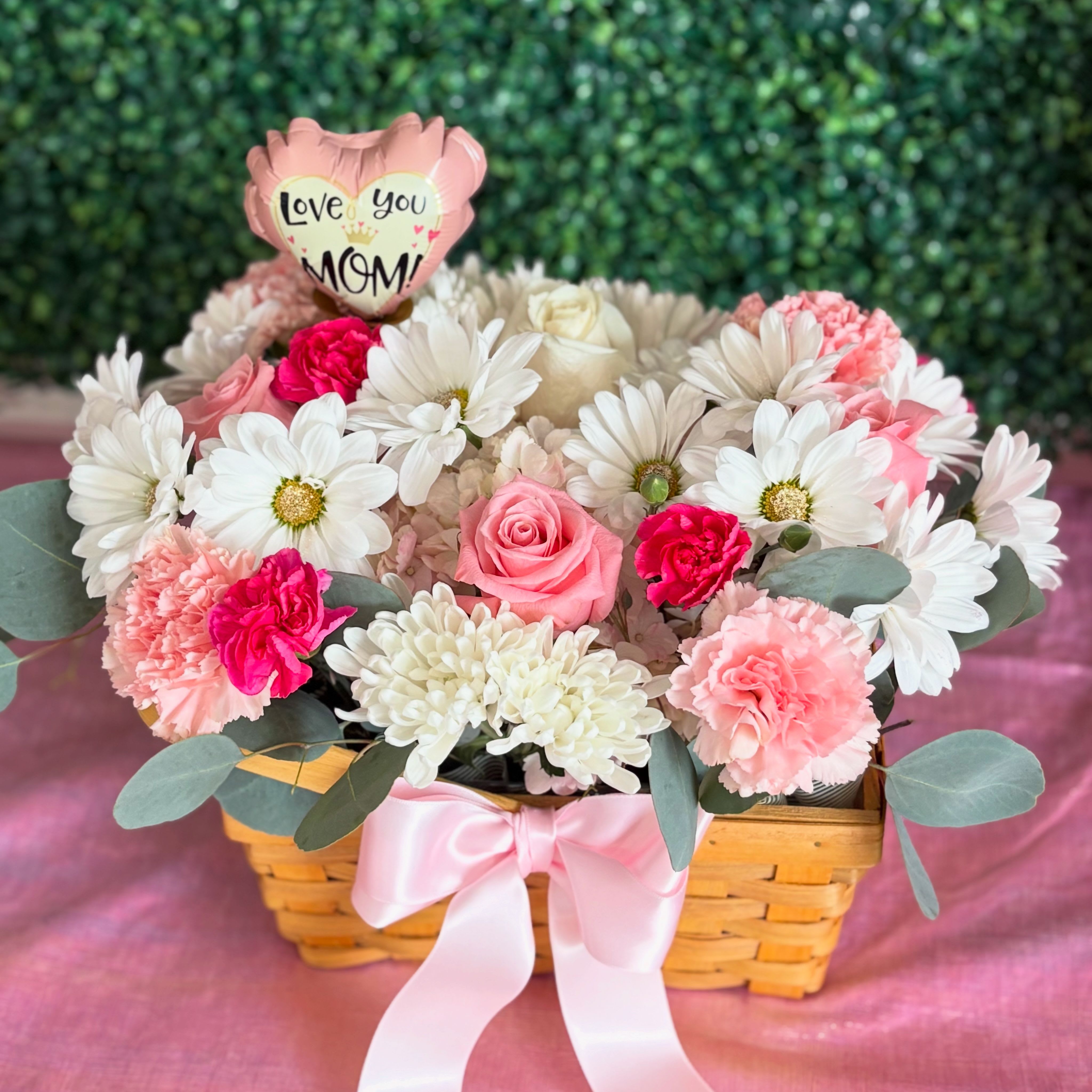 Mom Bloom Basket - Soft pastel pinks and crisp whites come together in a tender, gift-ready arrangement made especially for Mother's Day or any moment you want to celebrate a mom. This flower arrangement of roses, carnations, chrysanthemums and daisies sits in a low woven basket, topped with a heart-shaped "Love you Mom" balloon pick that instantly says what the flowers mean-appreciation, love, and a gentle celebration.  Care is simple: keep in a cool spot away from direct sun, refresh the water as needed, and these blooms will continue to bring warmth and joy to her room.