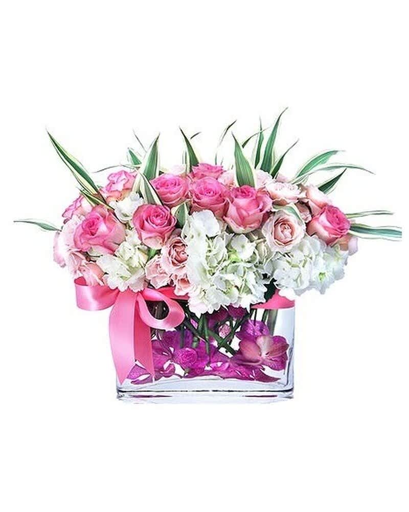 Low pink and white rose and hydrangea arrangement in a clear rectangular vase with pink ribbon