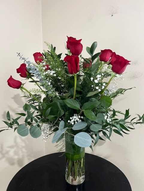 Tall arrangement of long-stem red roses with white filler flowers in a clear glass vase