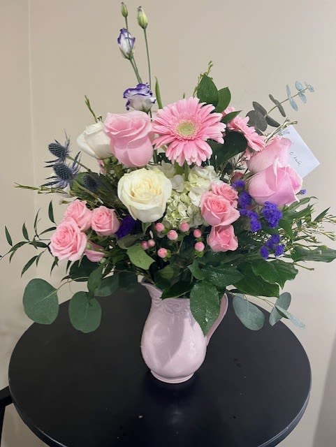 Pink and white mixed flower arrangement with purple accents in a pink ceramic pitcher.