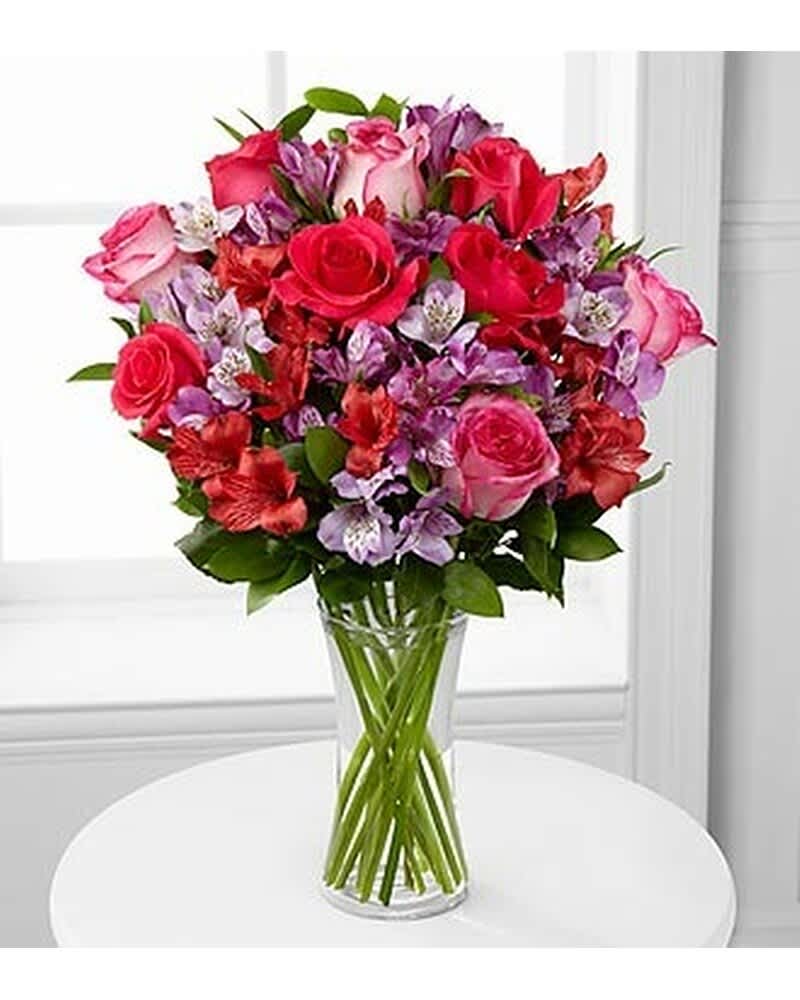 Tall glass vase of pink and red roses mixed with purple and white blooms
