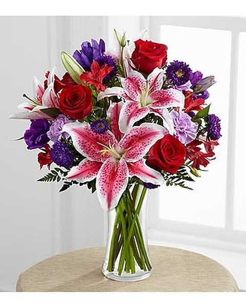 Stunning Beauty - The Stunning Beauty is an absolutely lovely way to send your love and affection across the miles. Fragrant Stargazer lilies stretch their star-like petals across a bed of rich red roses, lavender carnations, red Peruvian lilies, purple double lisianthus, purple matsumoto asters and lush greens. Beautifully arranged in a clear square tapered glass vase, these bouquets send your warmest sentiments with glamour and grace.