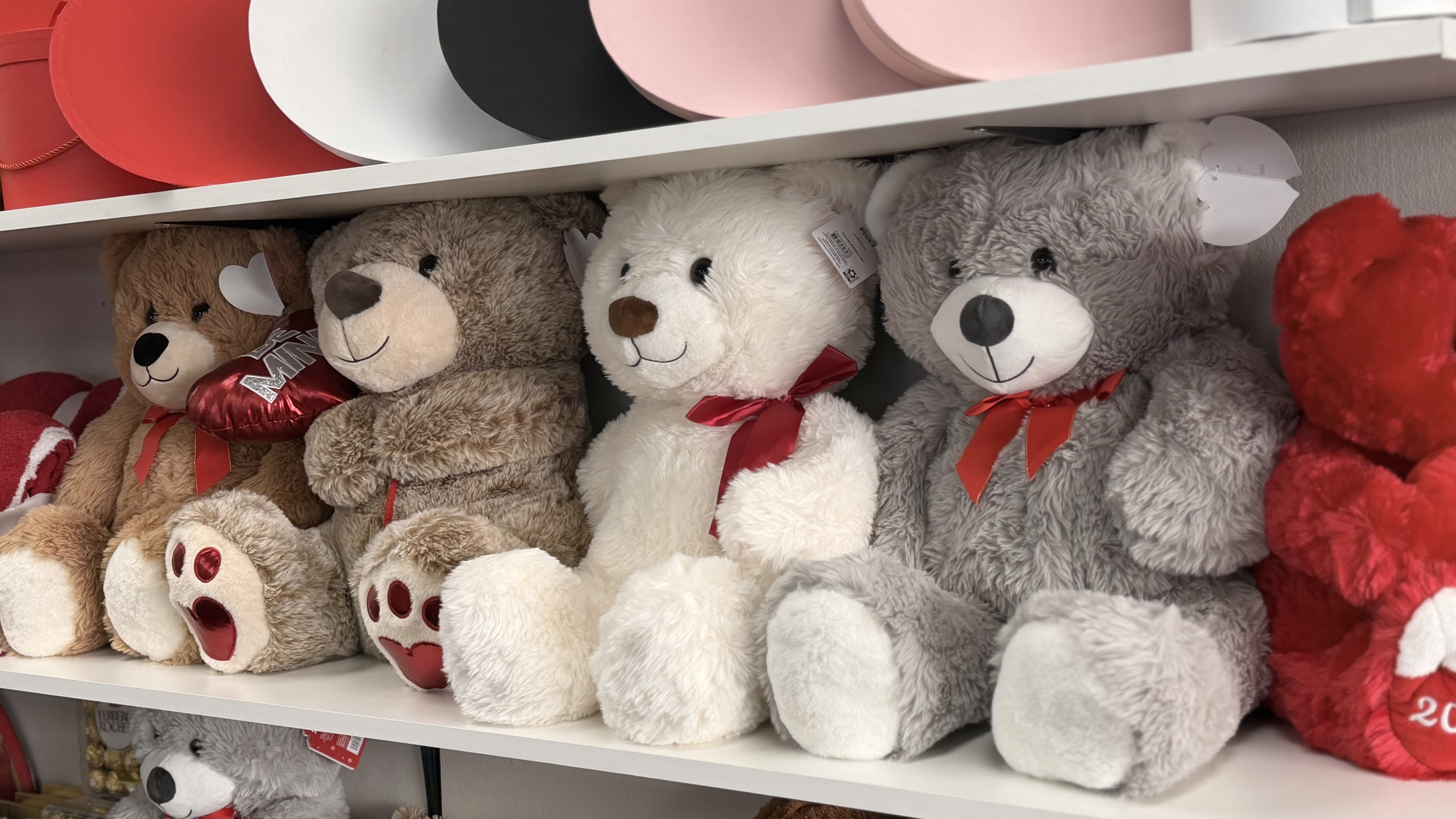 Row of plush teddy bears with red accents displayed on white shelves
