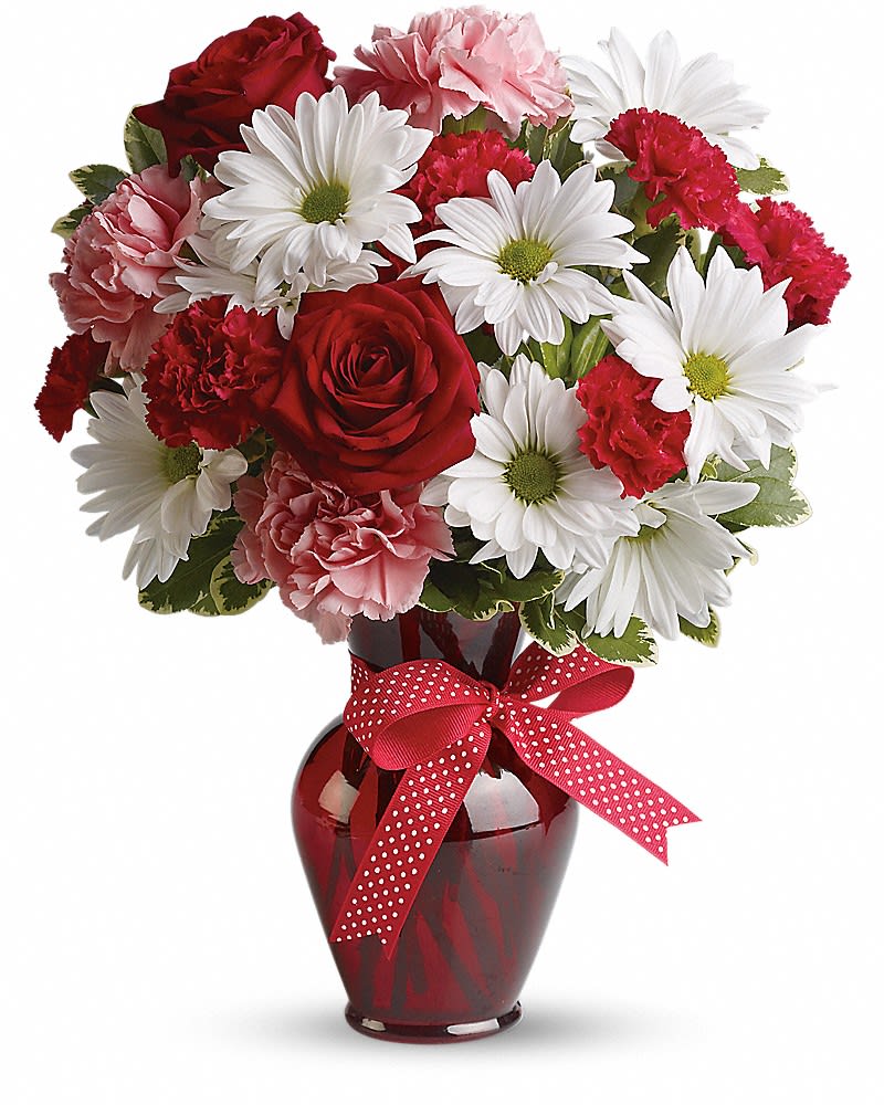Red and pink bouquet with roses, carnations, and white daisies in a red vase with a polka dot bow