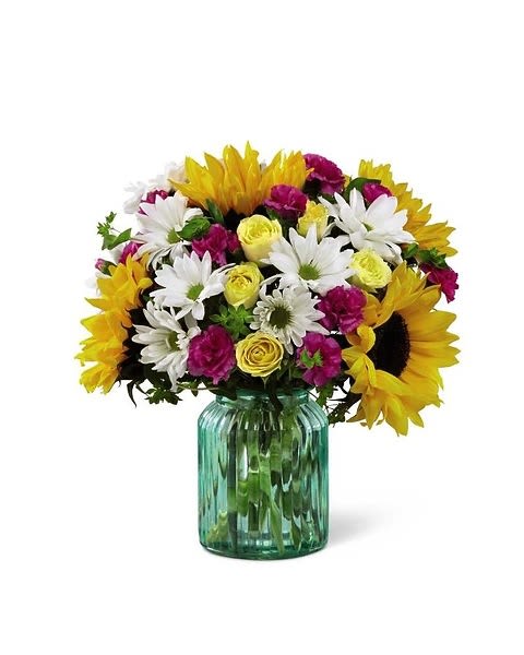 Sunlit Meadows - This simply lovely bouquet makes a terrific way to add color and country charm to any Mother's Day celebration. Its casual cheer and brilliant color palette comes from the combination of brilliant sunflowers, yellow spray roses, magenta mini carnations, white traditional daisies and lush green accents in an aqua blue canister glass vase. It's "fresh from the garden" look is perfect for celebrating special birthdays and other milestone events, or to express your "thanks" or "get well" wishes.  