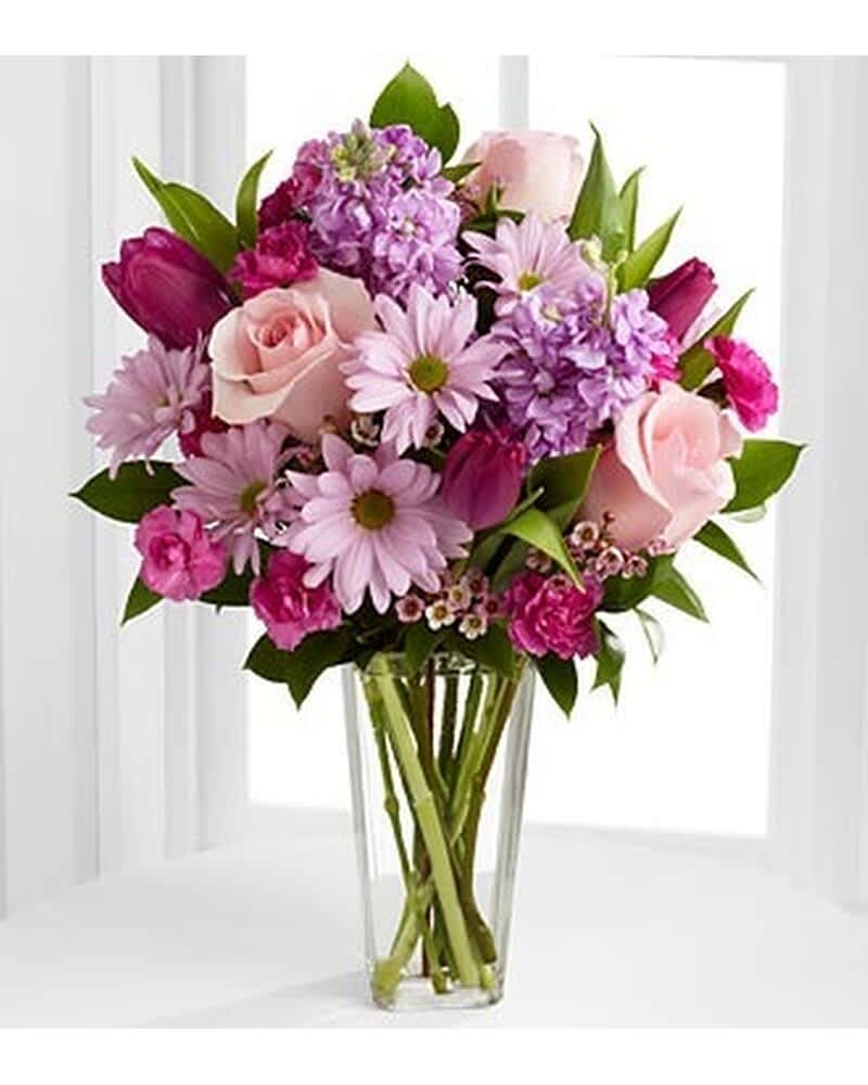 Mixed bouquet of pink roses, tulips, daisies, and stock in a tall clear glass vase