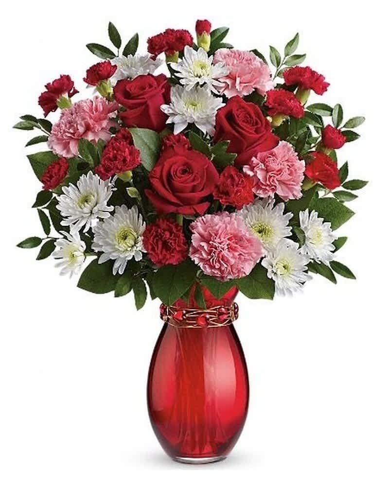 Arrangement of red roses, pink carnations, and white mums in a red glass vase