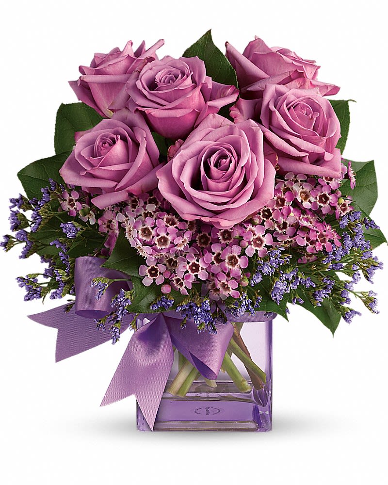 Lavender roses and pink filler flowers in a purple glass cube vase with matching ribbon.