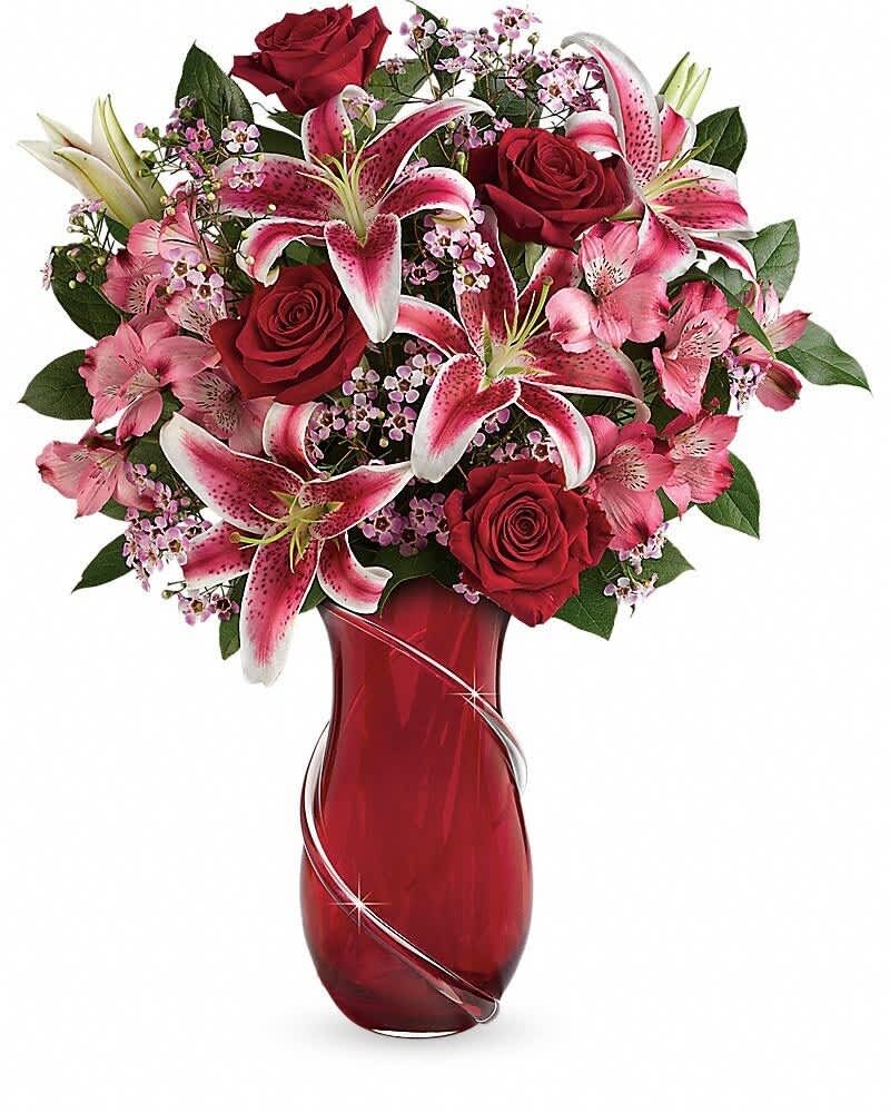 Red roses and pink lilies arranged in a red glass vase with silver swirl accents